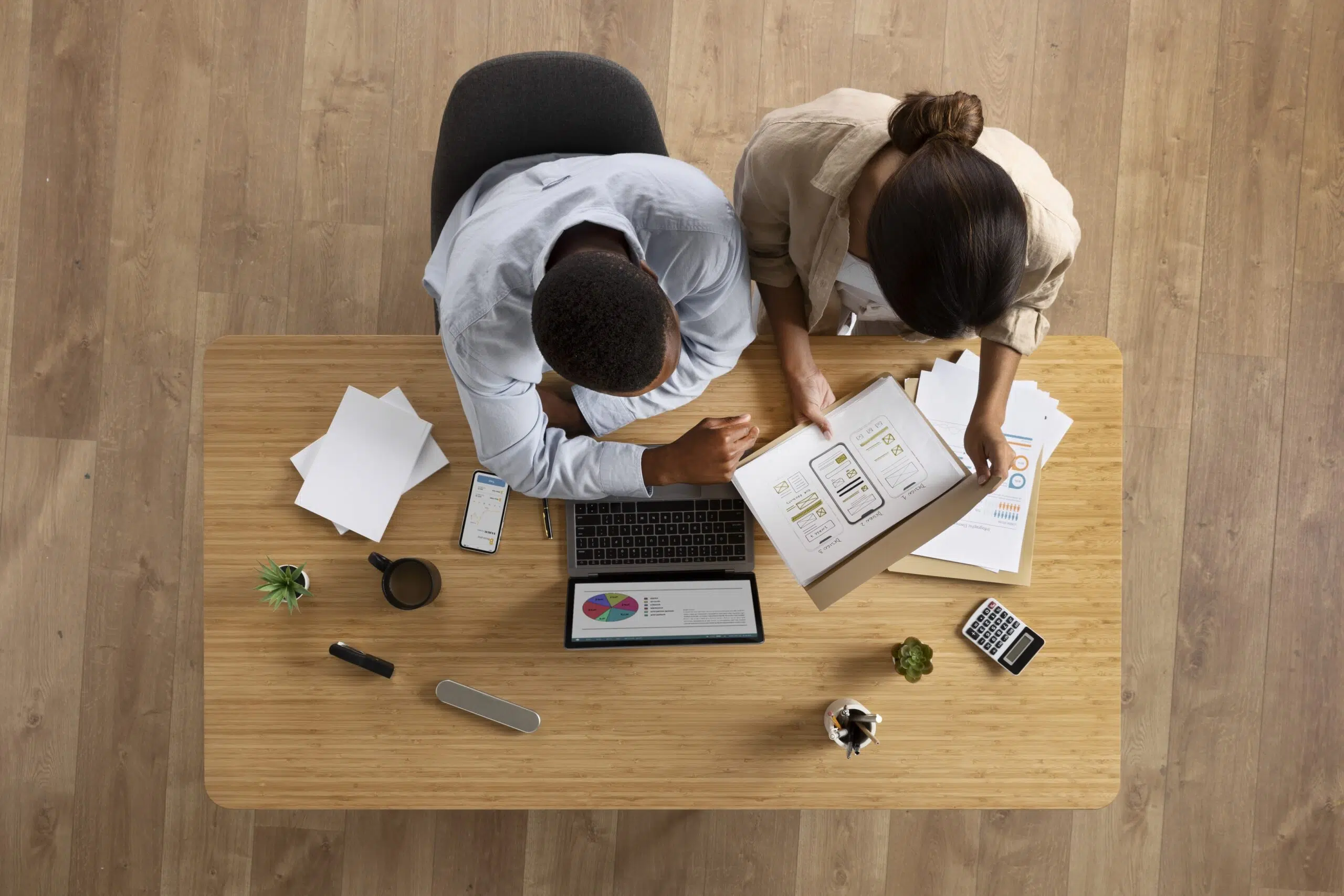 Top view of colleagues sitting next to each at a desk, looking at a laptop and documents.