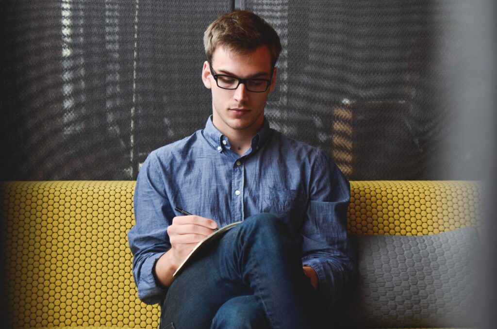 Young man wearing glasses sitting on yellow sofa with leg crossed writing in notepad - Full Federal Court ruling in the Bendel Case